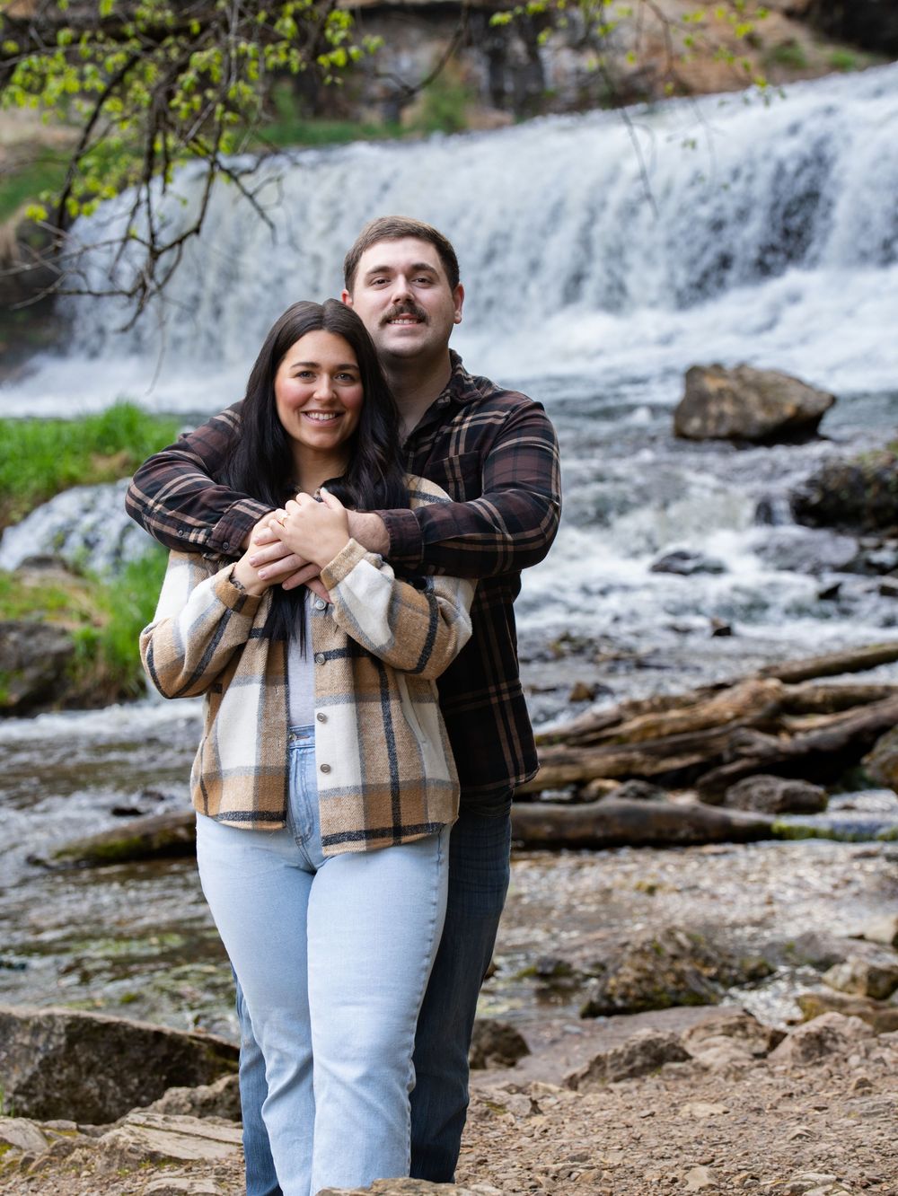 A couple embracing on the rocky bank below a waterfall in autumn