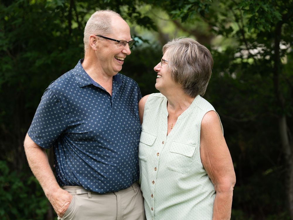 An older couple laughing and gazing at each other in a leafy garden