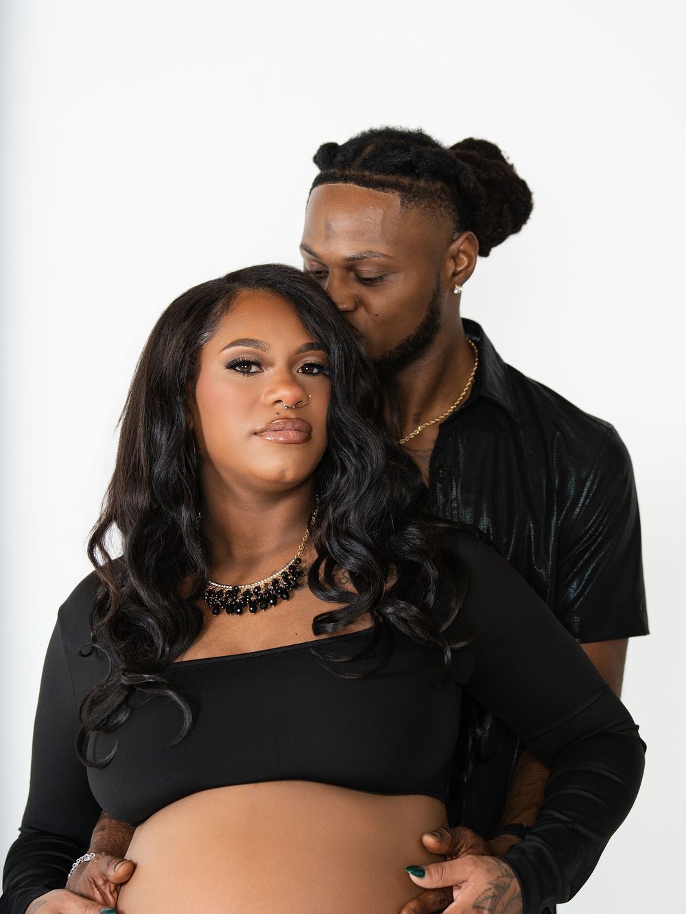 A man kissing a pregnant woman's head as he cradles her belly in a studio
