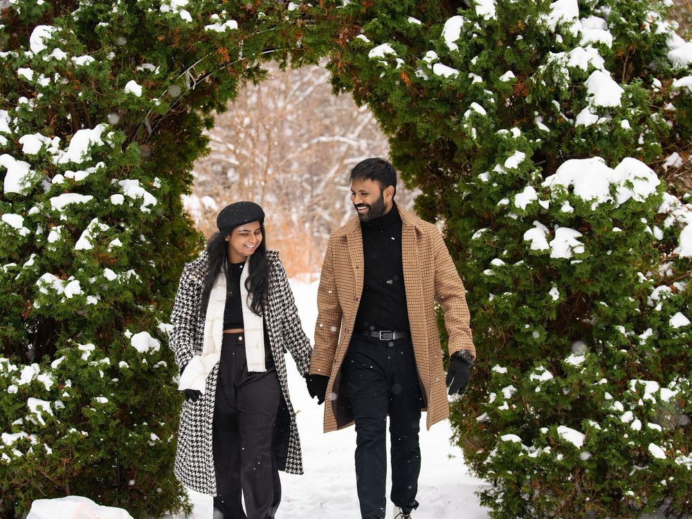 A couple walking hand in hand through a snow-covered evergreen archway