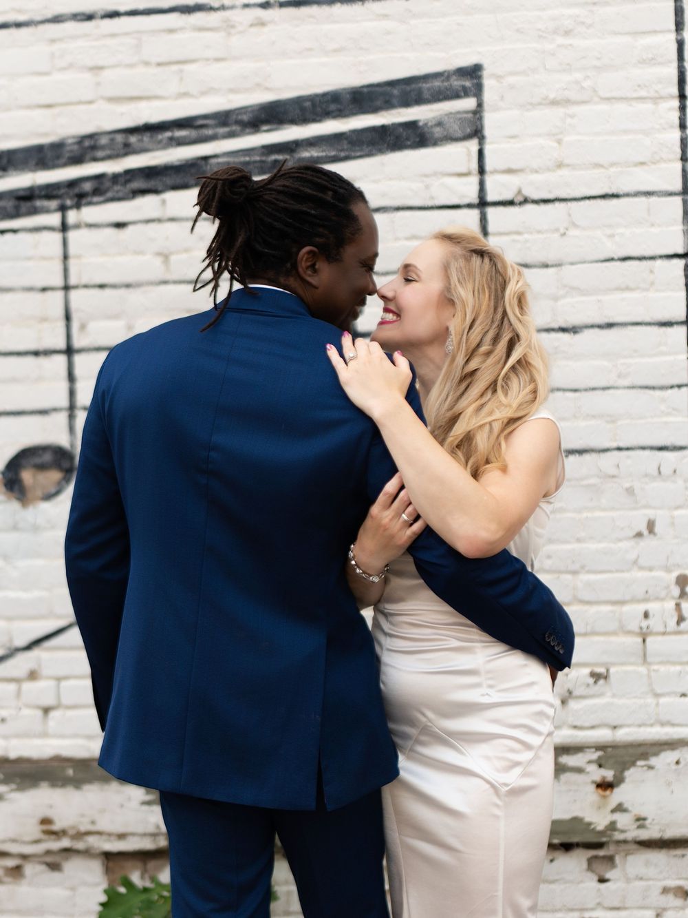 A couple in a close embrace against a whitewashed brick wall