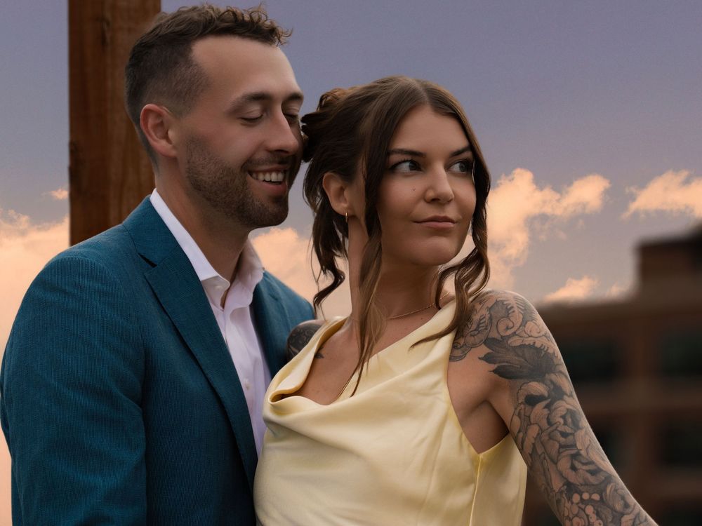 A couple sharing a quiet smile on a rooftop against a sunset sky