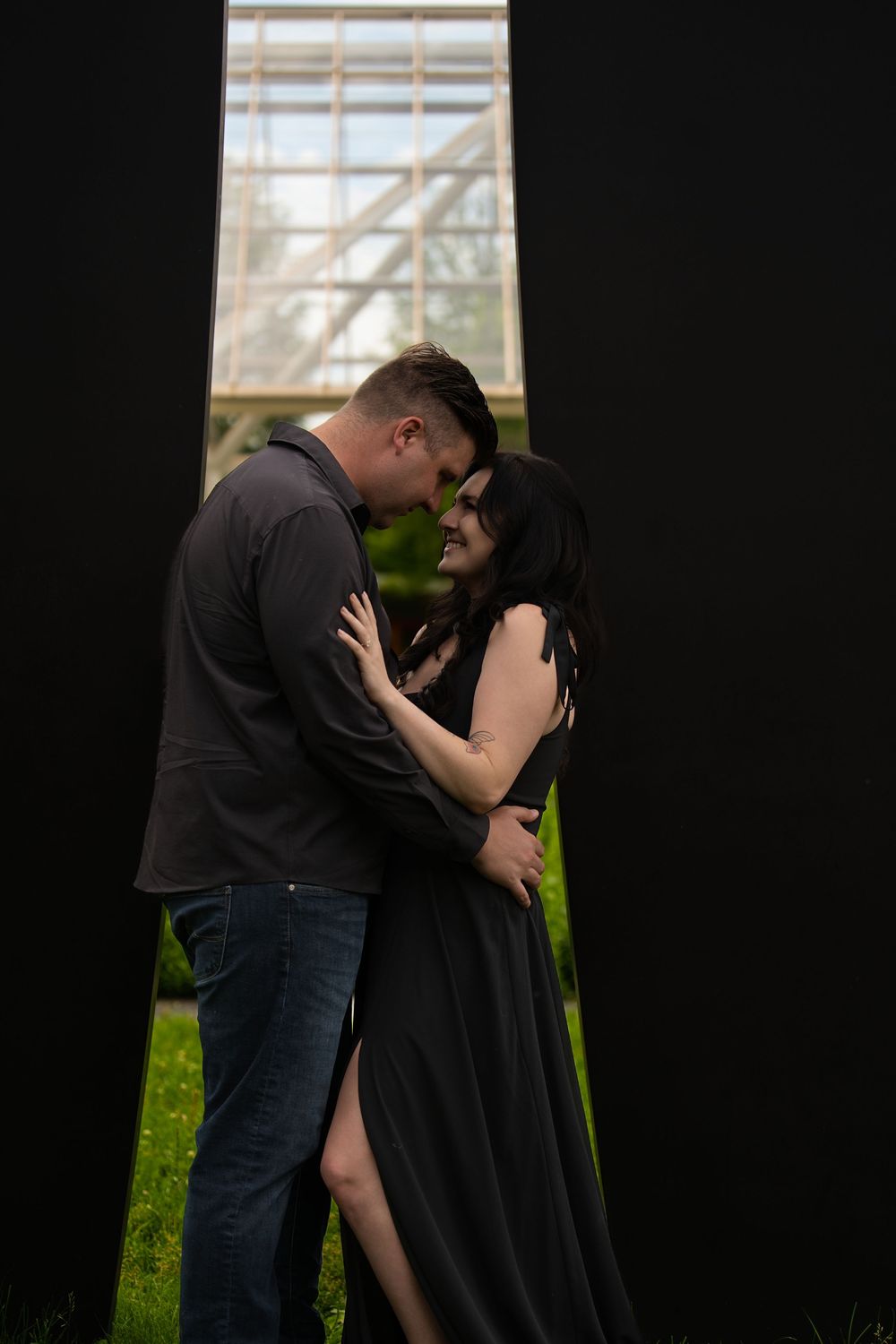 A couple embracing in a dark doorway with a glass conservatory glowing behind them
