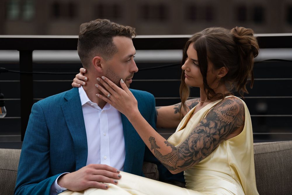 A woman touching a man's face as they sit close together on a rooftop sofa