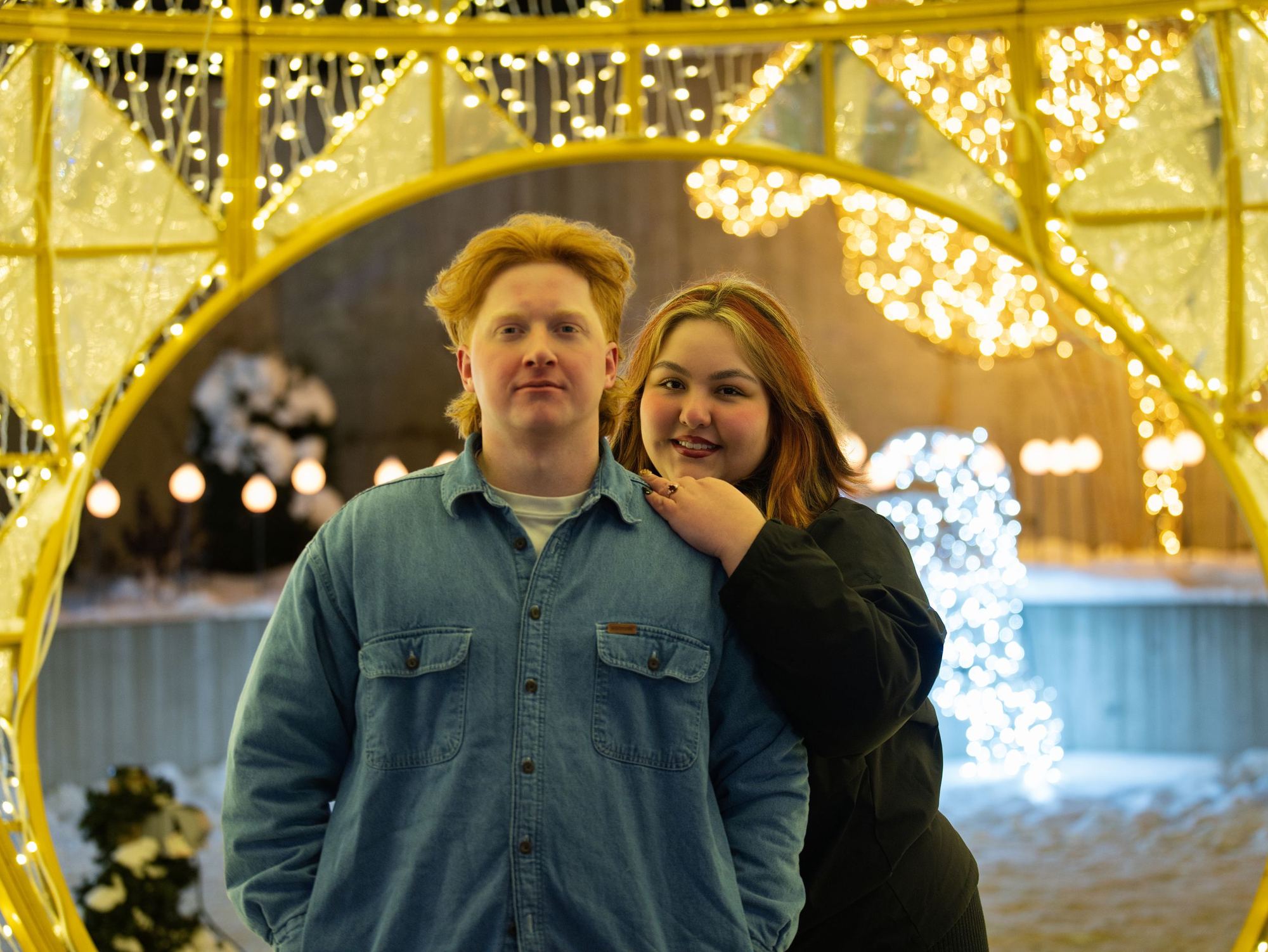 A couple posing inside a glowing golden tunnel at a holiday light display