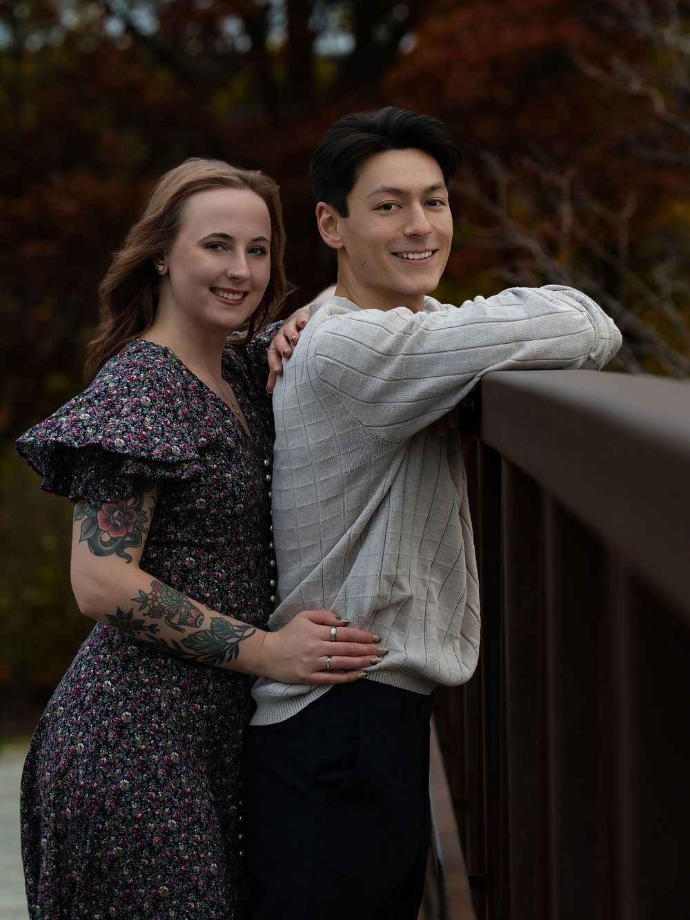 A couple leaning together on a wooden bridge rail among autumn trees