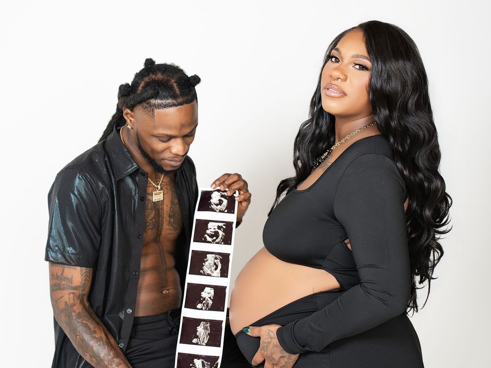 An expectant couple holding up a strip of ultrasound photos in a white studio