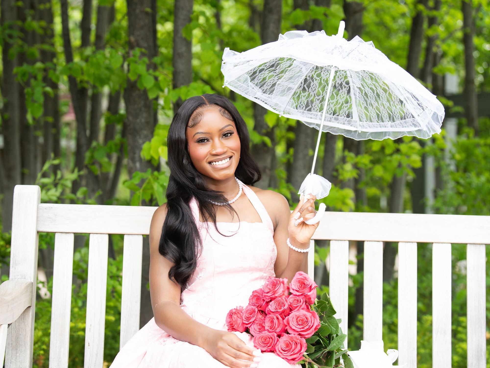 A young woman in a pink dress holding roses and a lace parasol on a garden bench