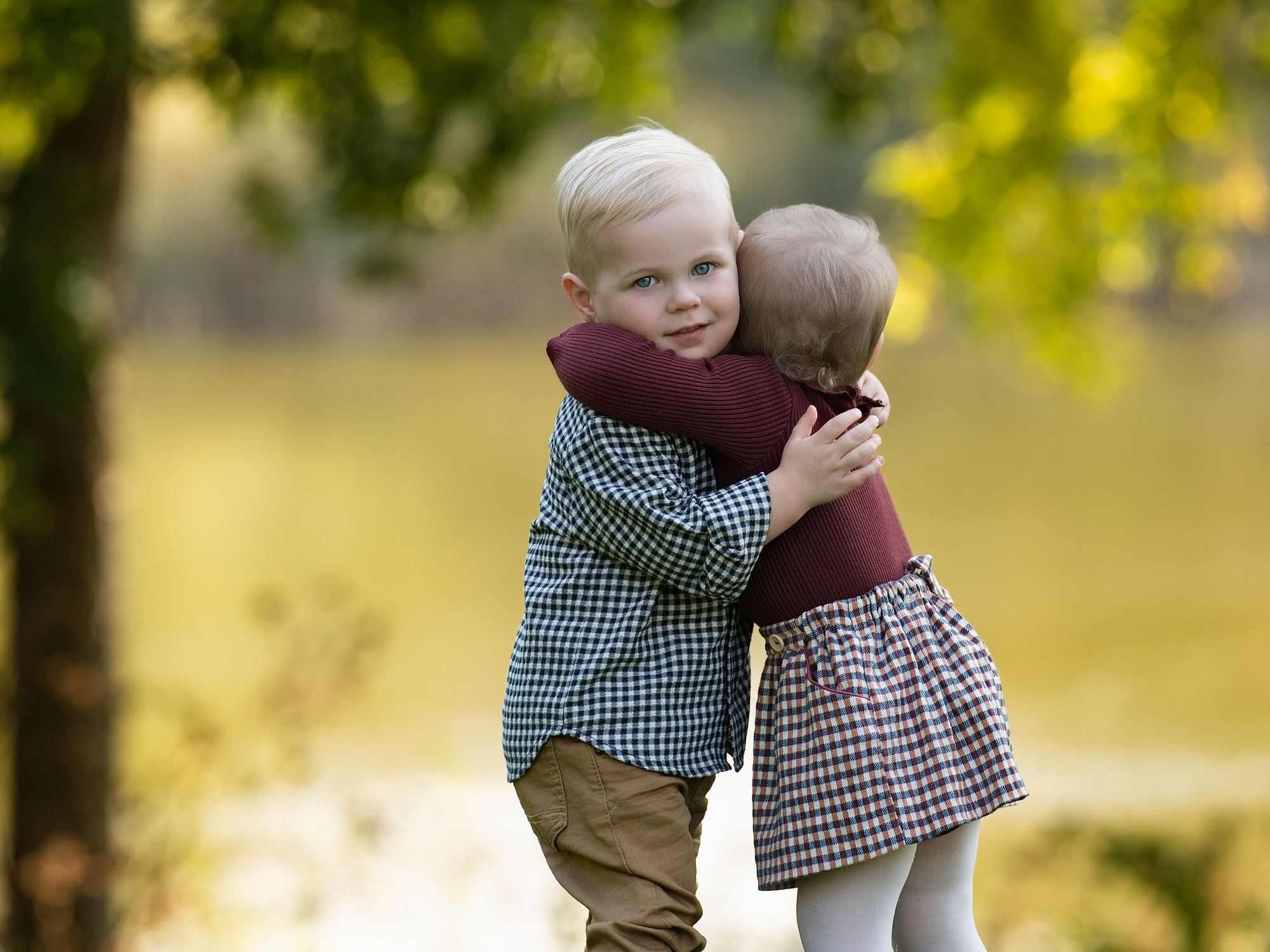 Two toddlers sharing a hug outdoors in warm golden autumn light