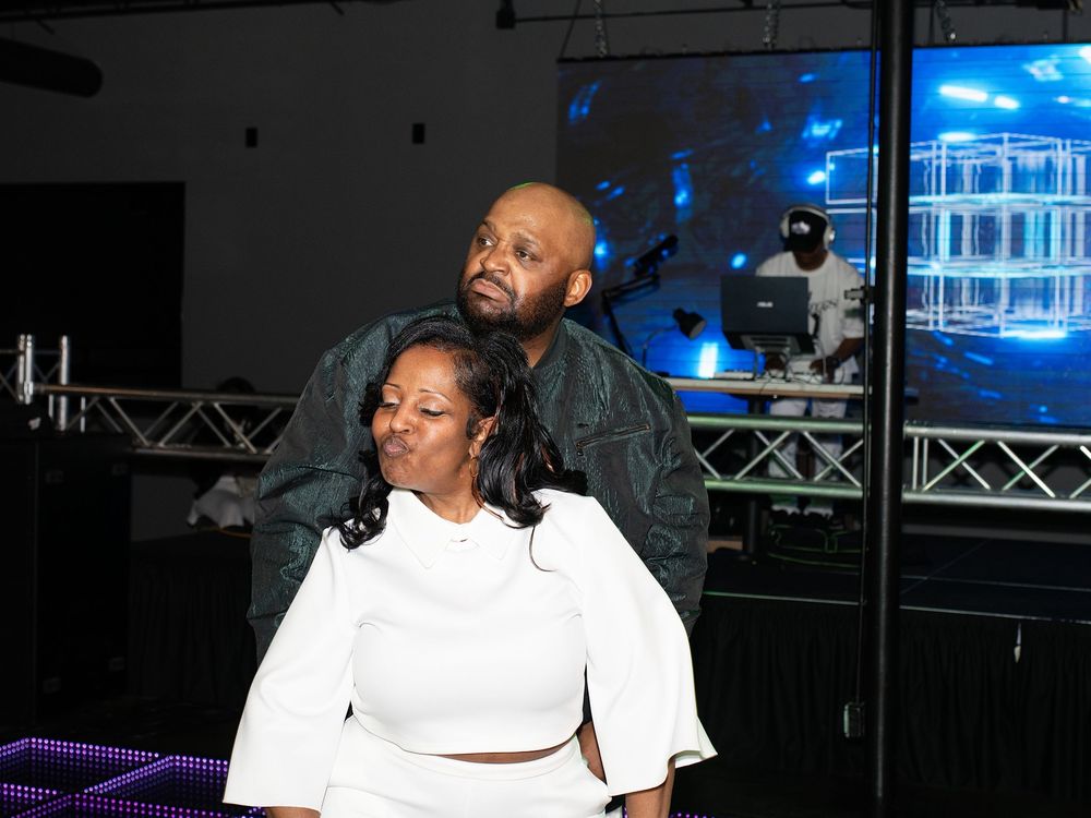 A couple posing playfully on a dance floor in front of a DJ booth at a party