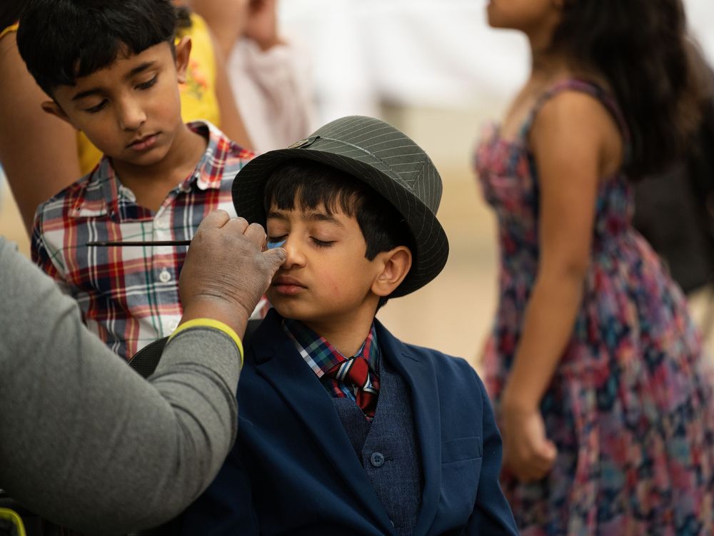A face painter decorating a young boy in a fedora at a family event
