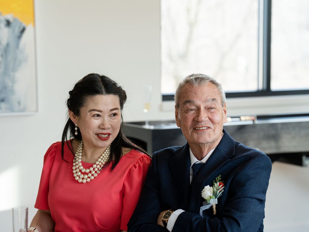 An older couple smiling side by side at an intimate celebration, the man wearing a boutonniere