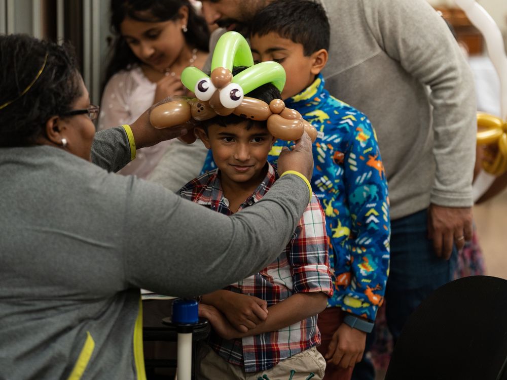 A balloon artist placing a balloon hat on a smiling boy's head at a party
