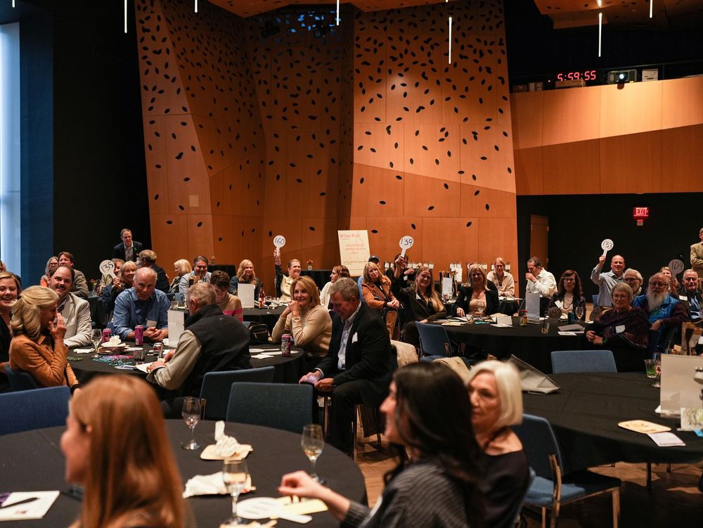 Guests seated at round tables raising bid paddles during a fundraising auction in a banquet hall