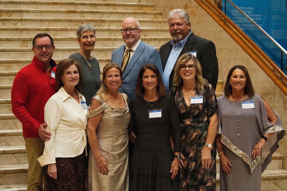 A group of guests in formal attire posing on a grand staircase at a gala
