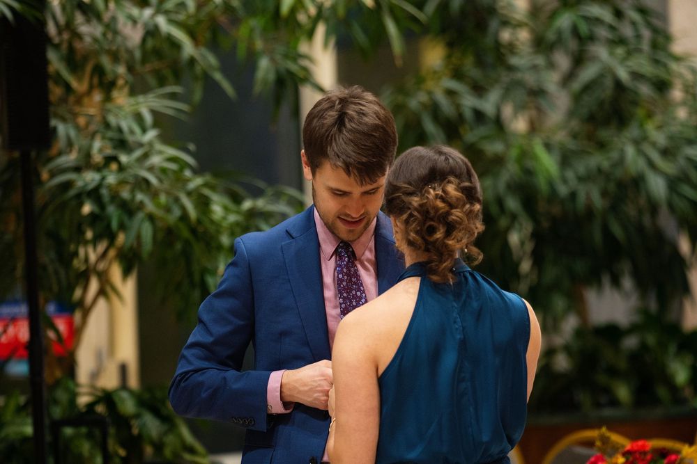 A woman helping a man adjust his suit jacket in a plant-filled atrium