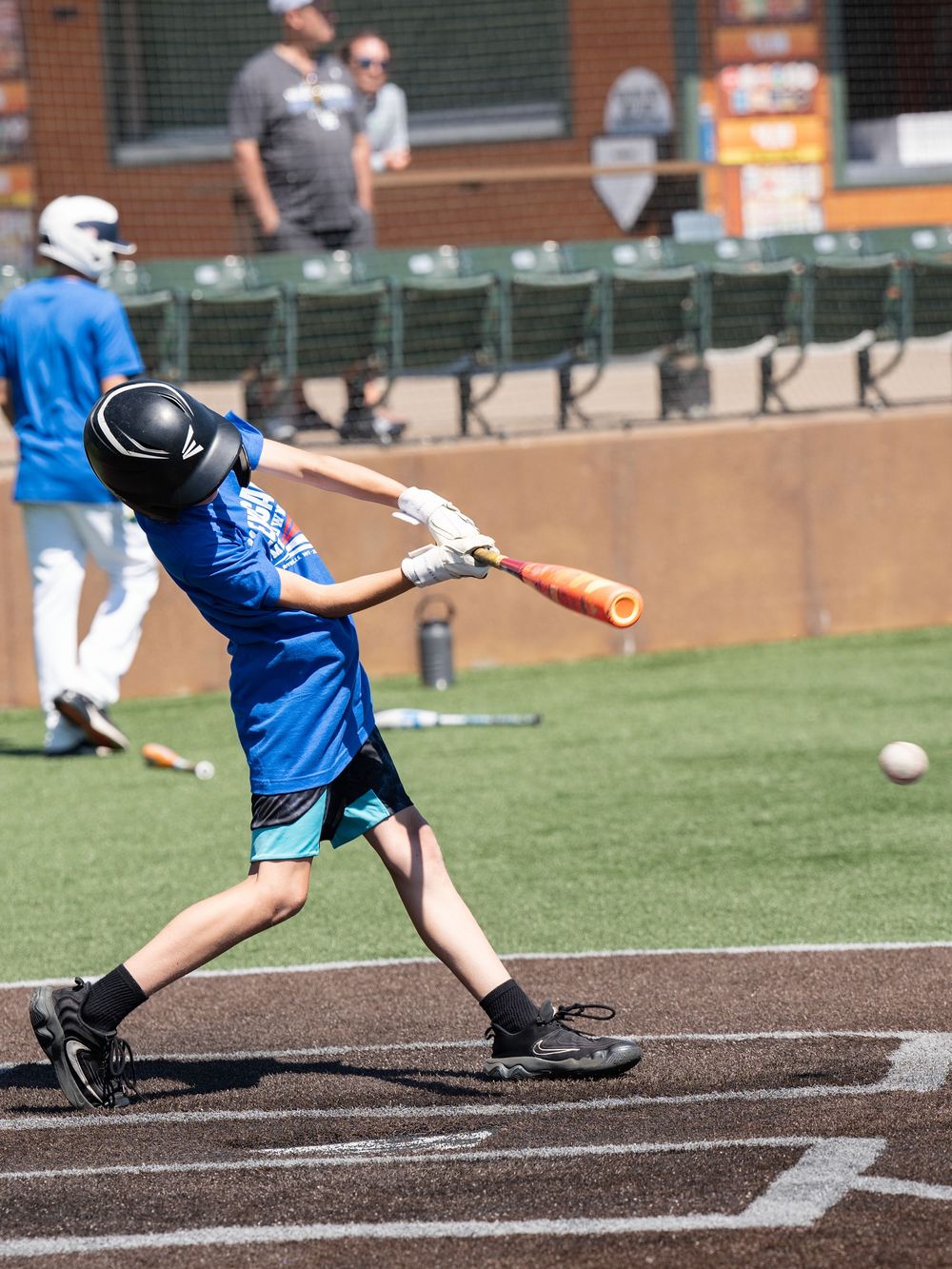 A young batter in a blue jersey swinging at a ball on a ballpark field