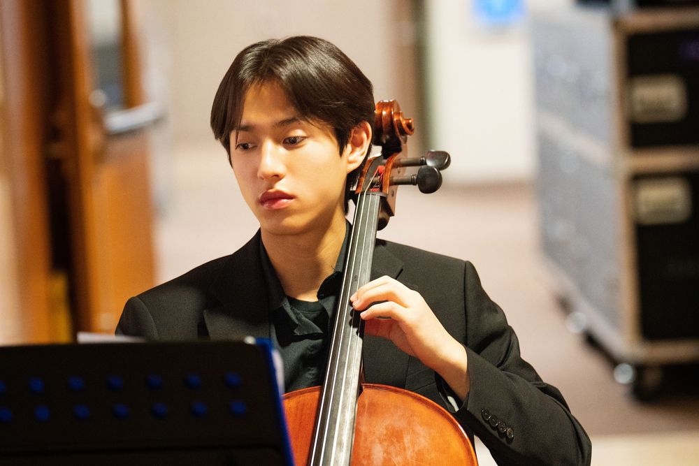 A young man in a dark suit playing the cello during a performance