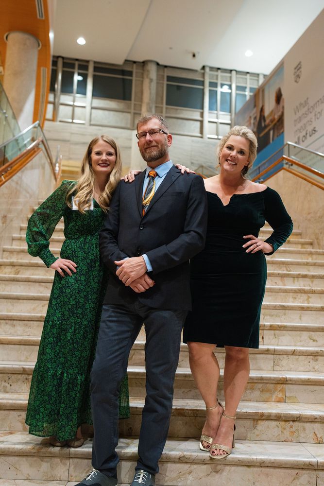 Three guests in formal wear posing on a marble staircase at a gala