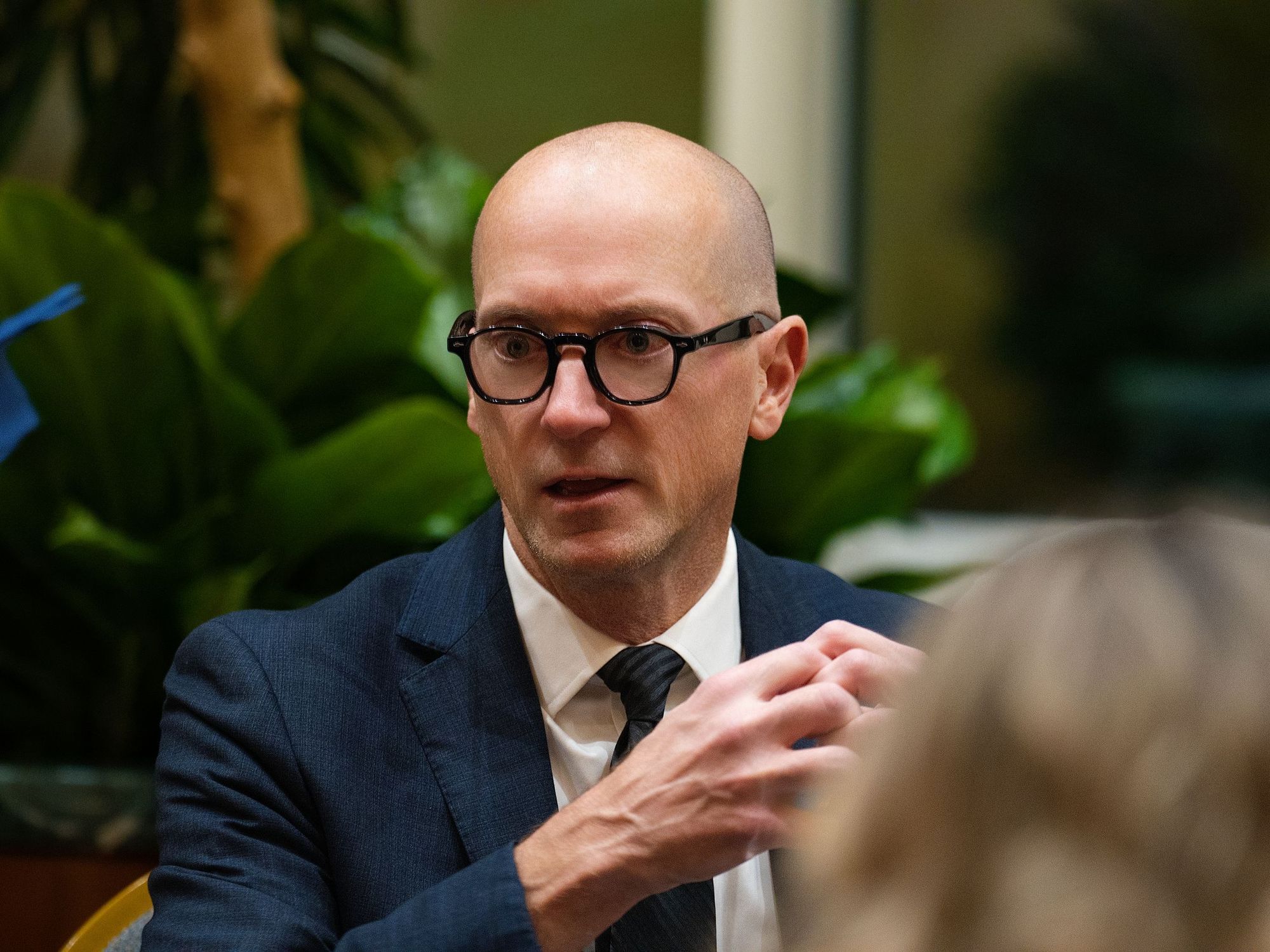 A man in glasses and a suit mid-conversation at a corporate event