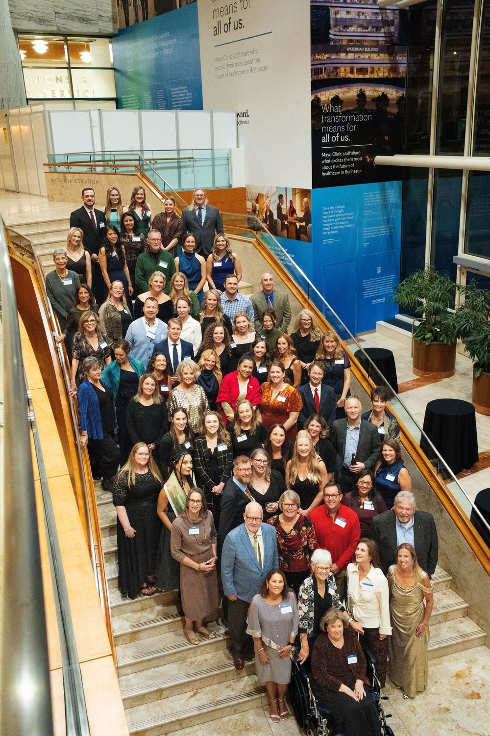 A large group in formal attire posing on a wide staircase at a gala