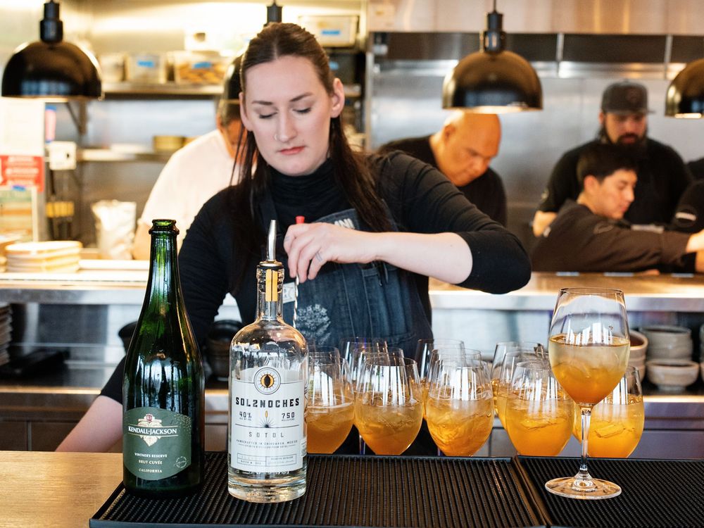 A bartender preparing cocktails at a bar lined with orange drinks and bottles