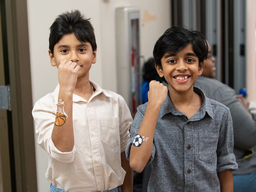 Two boys holding up arms painted with sports ball designs at a party