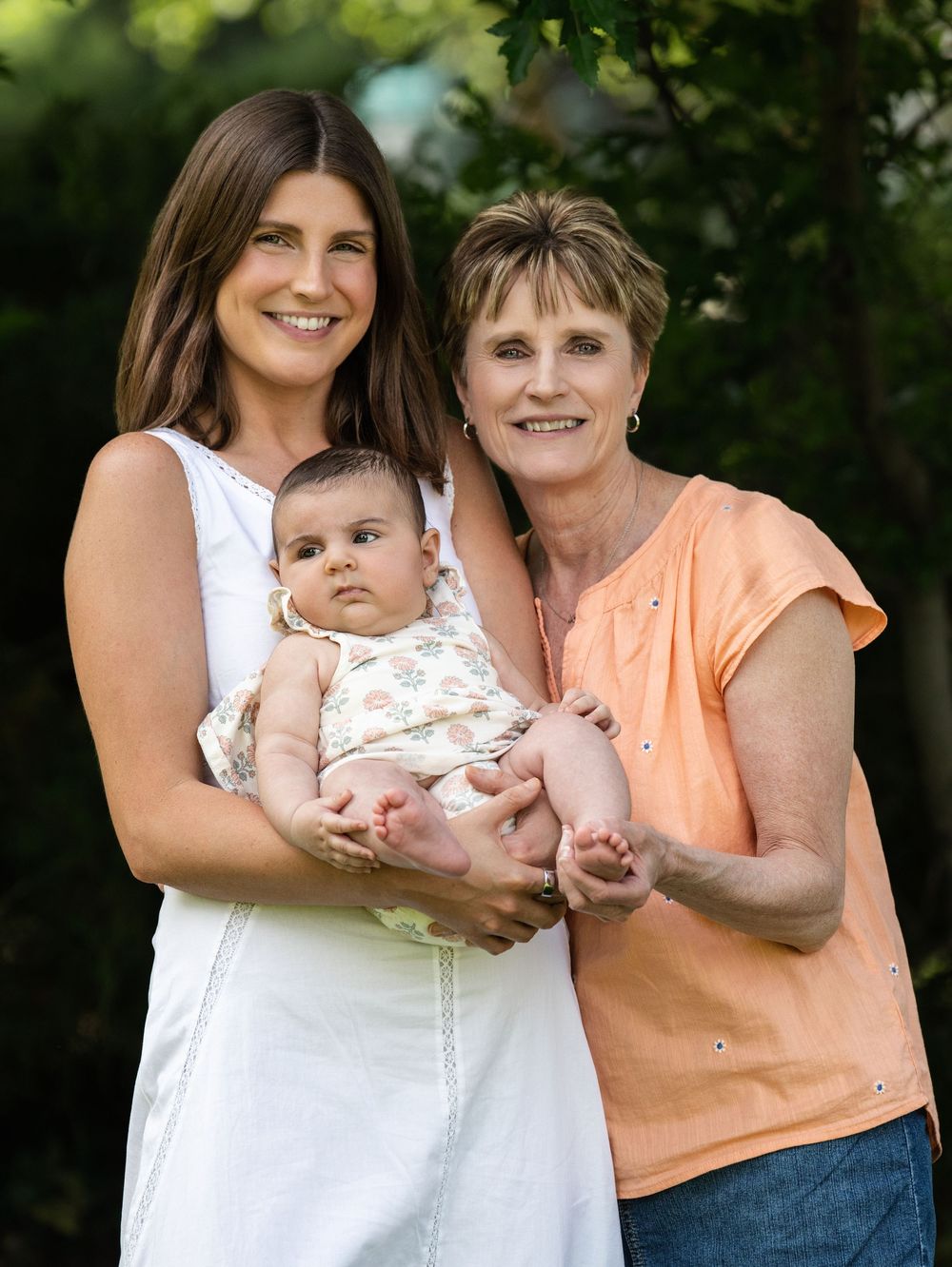 A woman holding a baby beside an older woman in a leafy garden