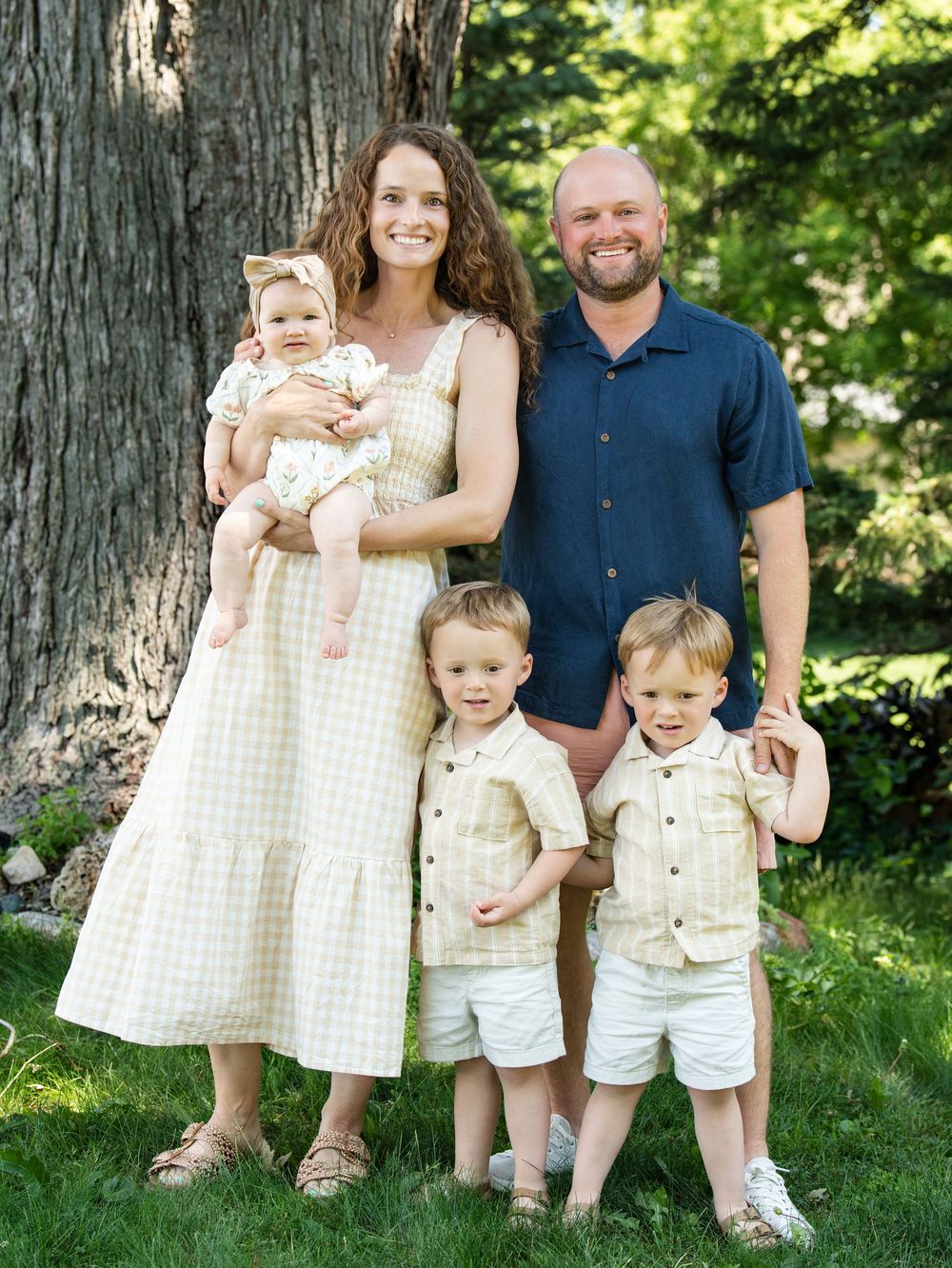 Parents with a baby and two young boys posing under a large tree