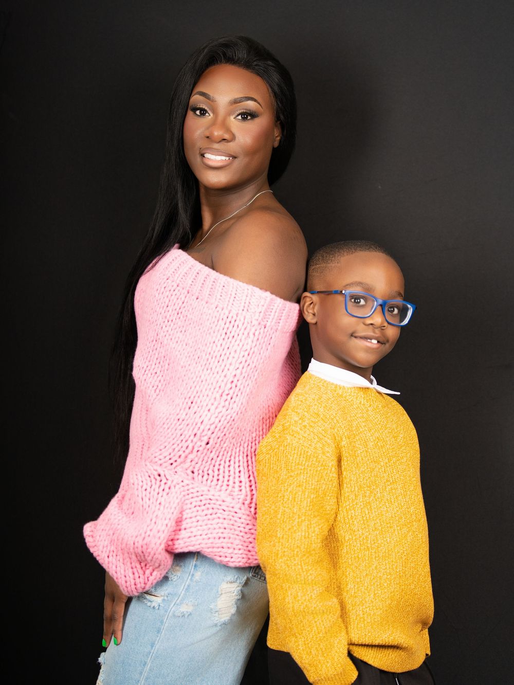 A woman and a young boy in a yellow sweater posing against a dark studio backdrop