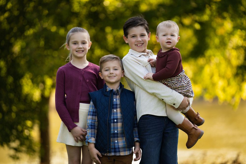 Four children posing among golden autumn trees, the oldest boy holding a toddler