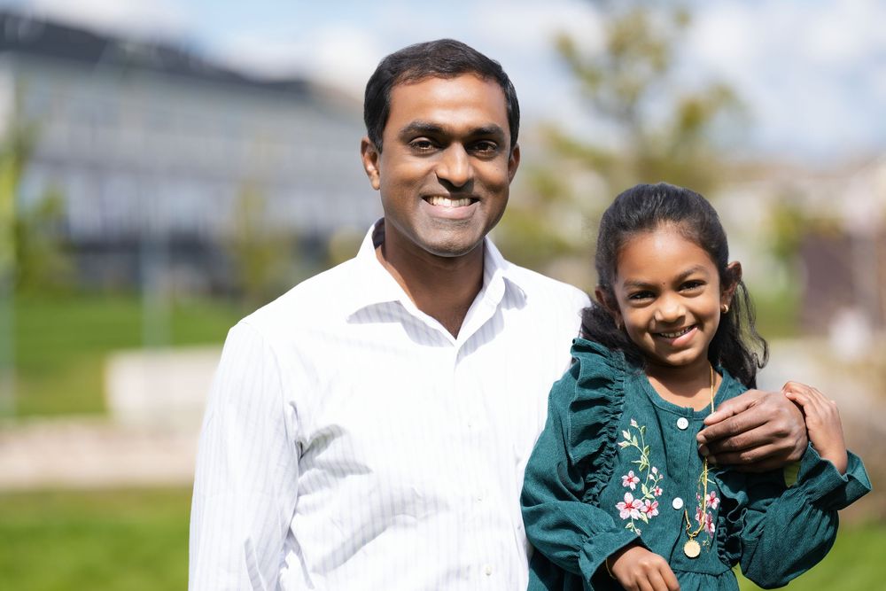 A man and a young girl smiling side by side in a sunny park