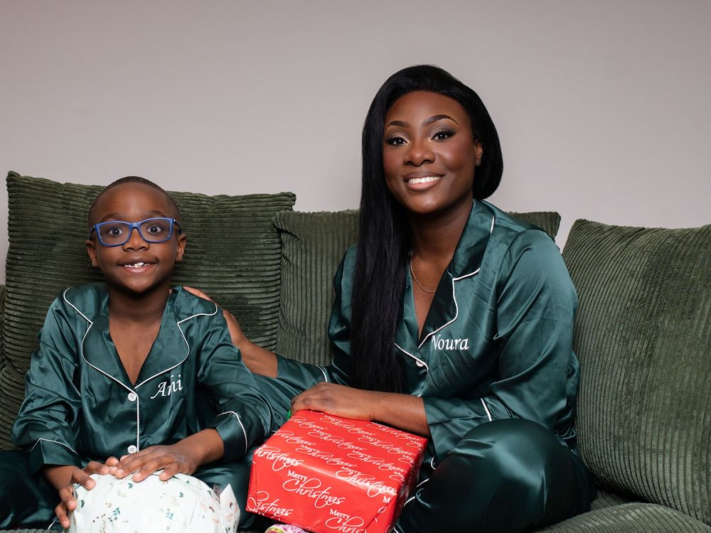 A woman and a young boy in matching green pajamas opening gifts on a sofa