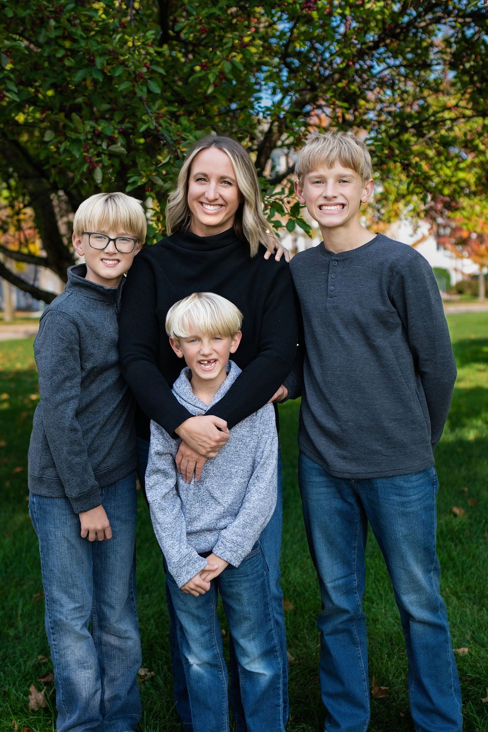 A woman posing on a lawn with three boys in blue and grey sweaters