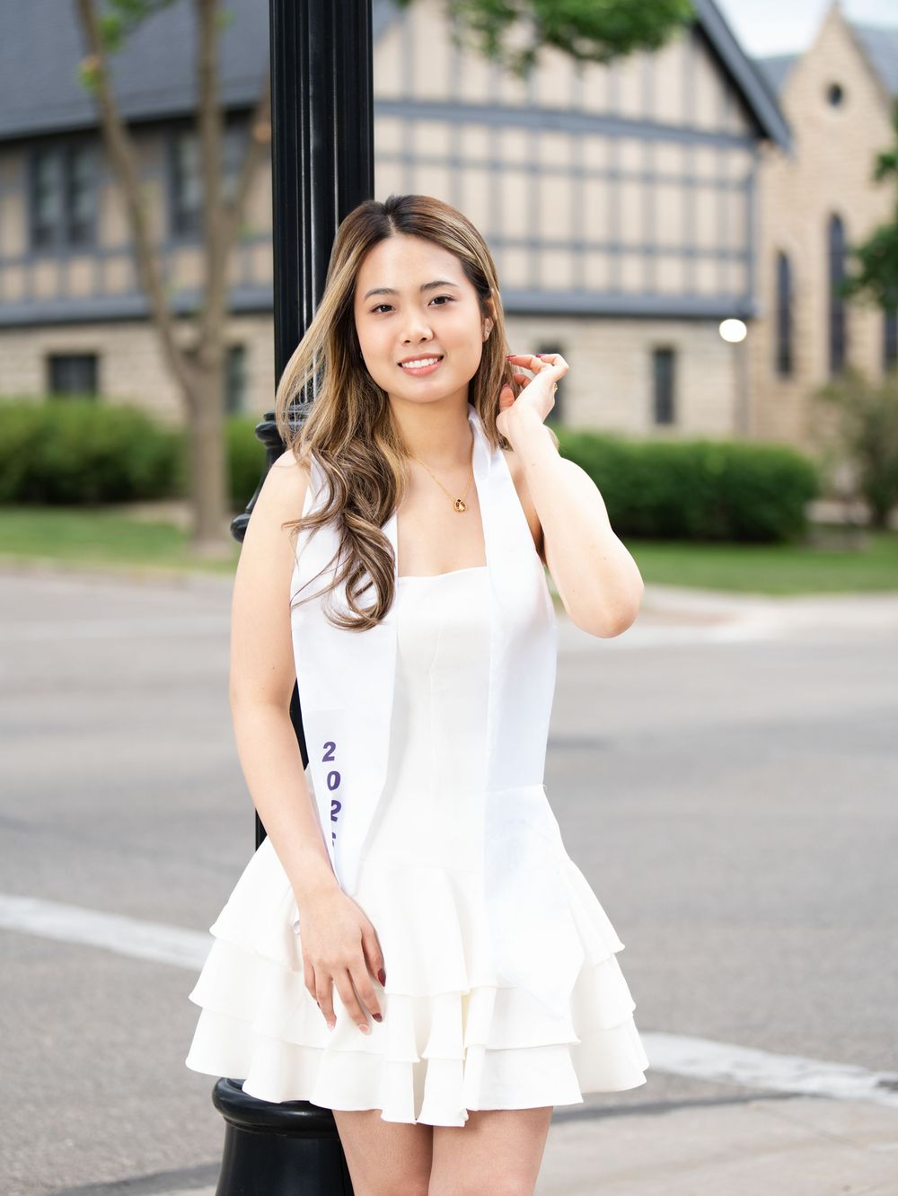 A graduate in a white dress and stole posing on a city street corner