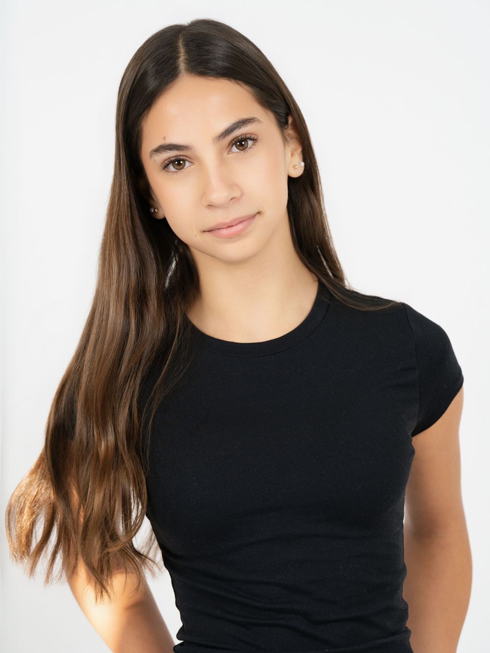 A young woman with long brown hair in a black T-shirt against a white studio backdrop
