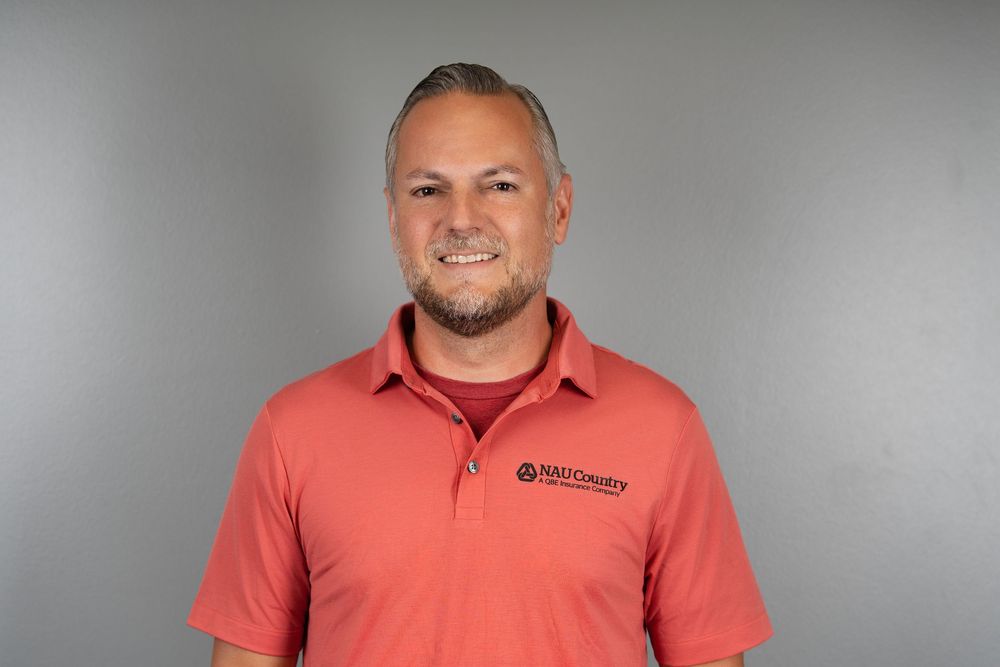 A smiling man in a coral polo shirt against a grey studio backdrop