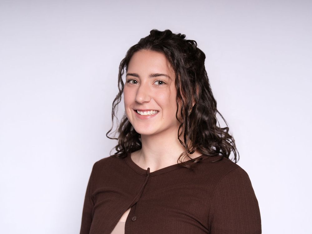 A smiling woman with long curly hair in a brown cardigan against a light studio backdrop