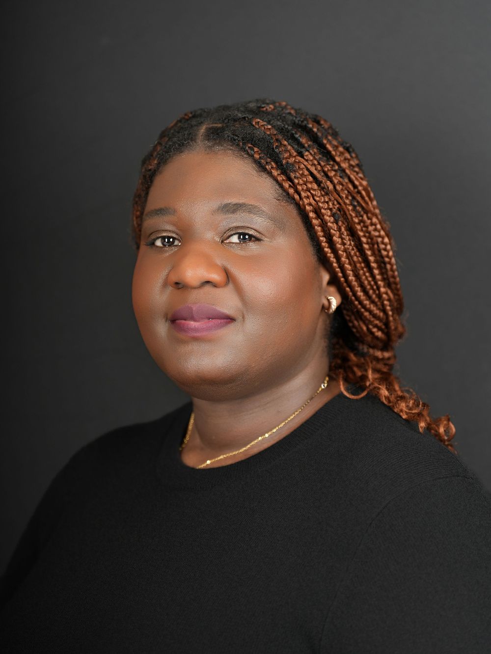 A woman with long braids in a black top against a dark grey studio backdrop