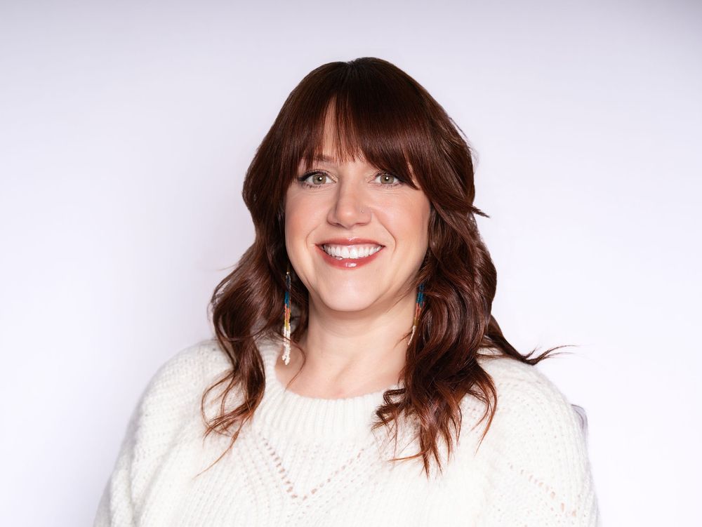 A smiling woman with auburn hair and bangs in a cream sweater against a light studio backdrop