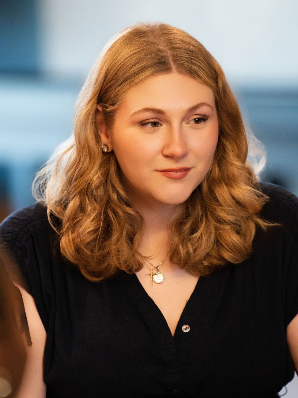 A young woman with wavy auburn hair in a black top gazing off to the side indoors