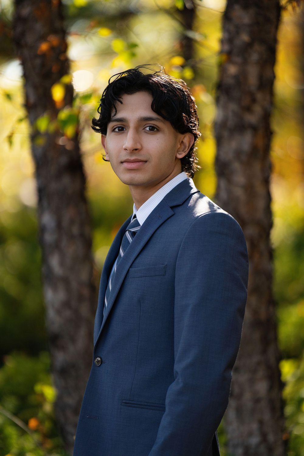 A young man in a navy suit and tie standing among autumn trees
