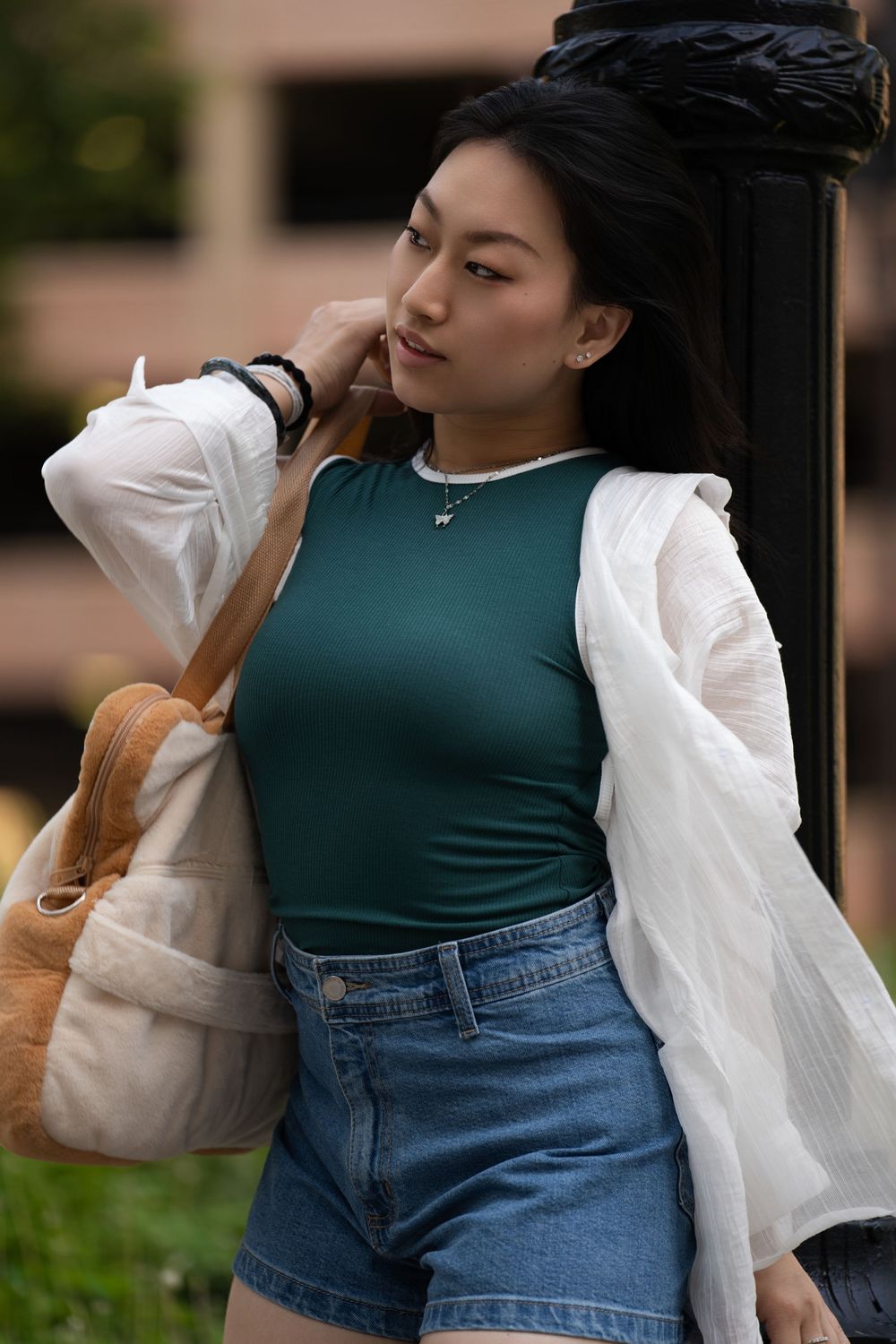 A young woman in a green top and denim shorts poses with a tote bag outdoors