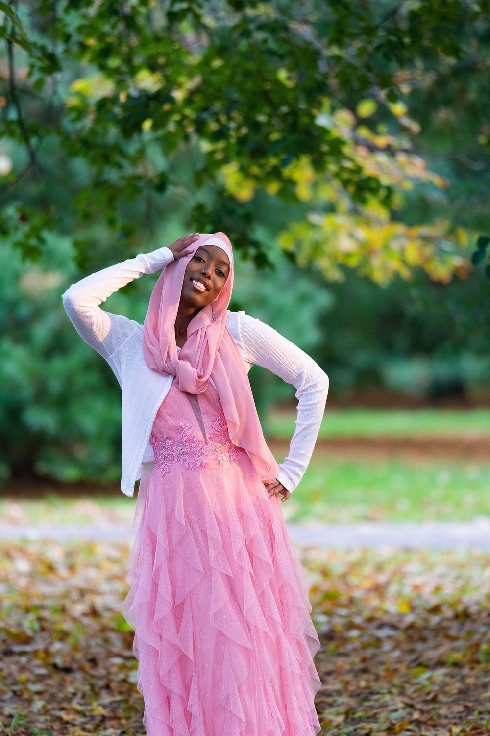 A young woman in a pink tulle dress and pink headscarf poses in an autumn park