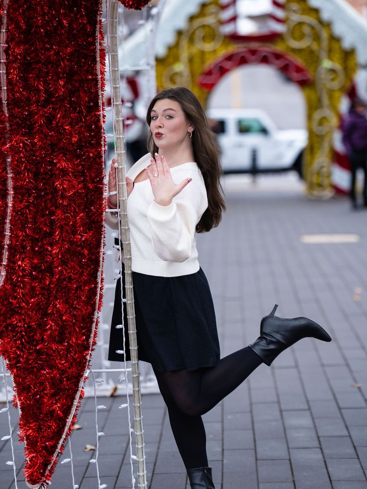 A woman shows off her engagement ring with a playful pose among festive holiday decorations