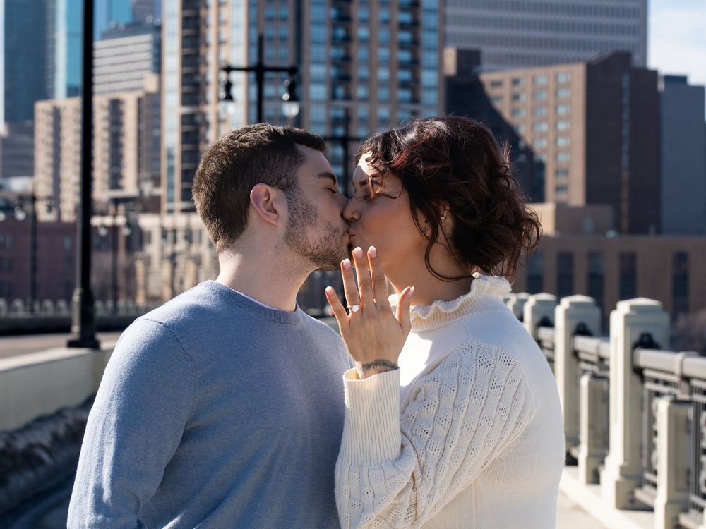 A newly engaged couple kisses as the woman shows her ring on a city bridge