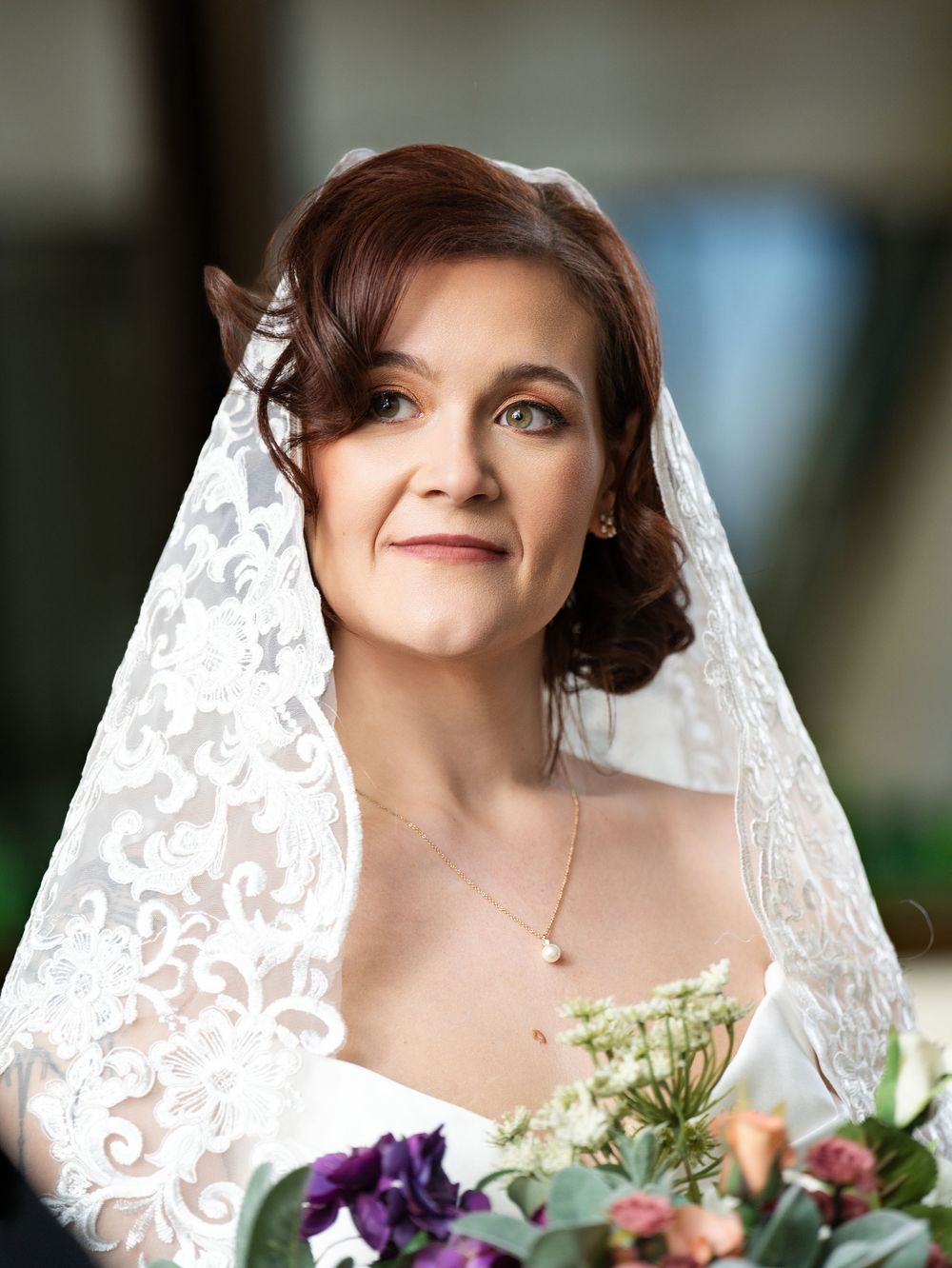 A bride in a lace-edged veil holds a bouquet in a close portrait
