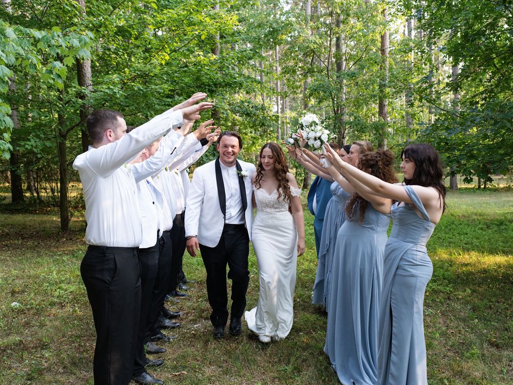 A bride and groom walk through an arch of cheering bridesmaids and groomsmen in the woods