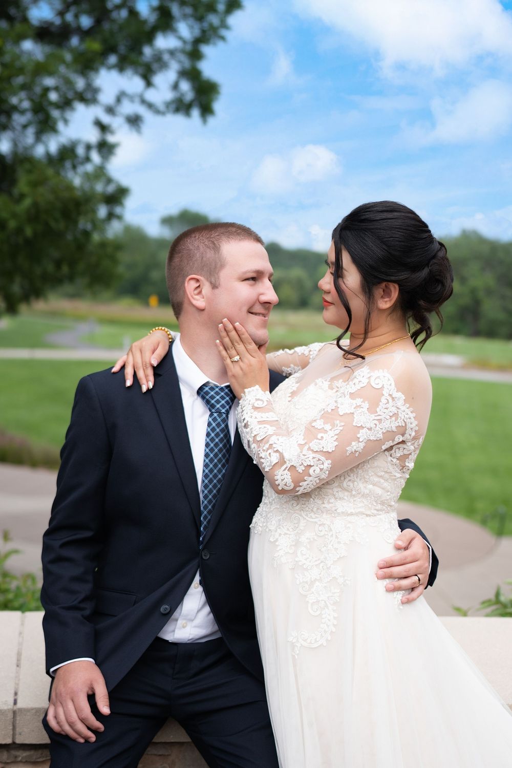 A bride touches the groom's face as they share a close moment on a garden path