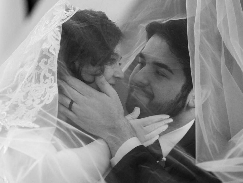 A bride and groom share a tender moment under her lace veil in black and white